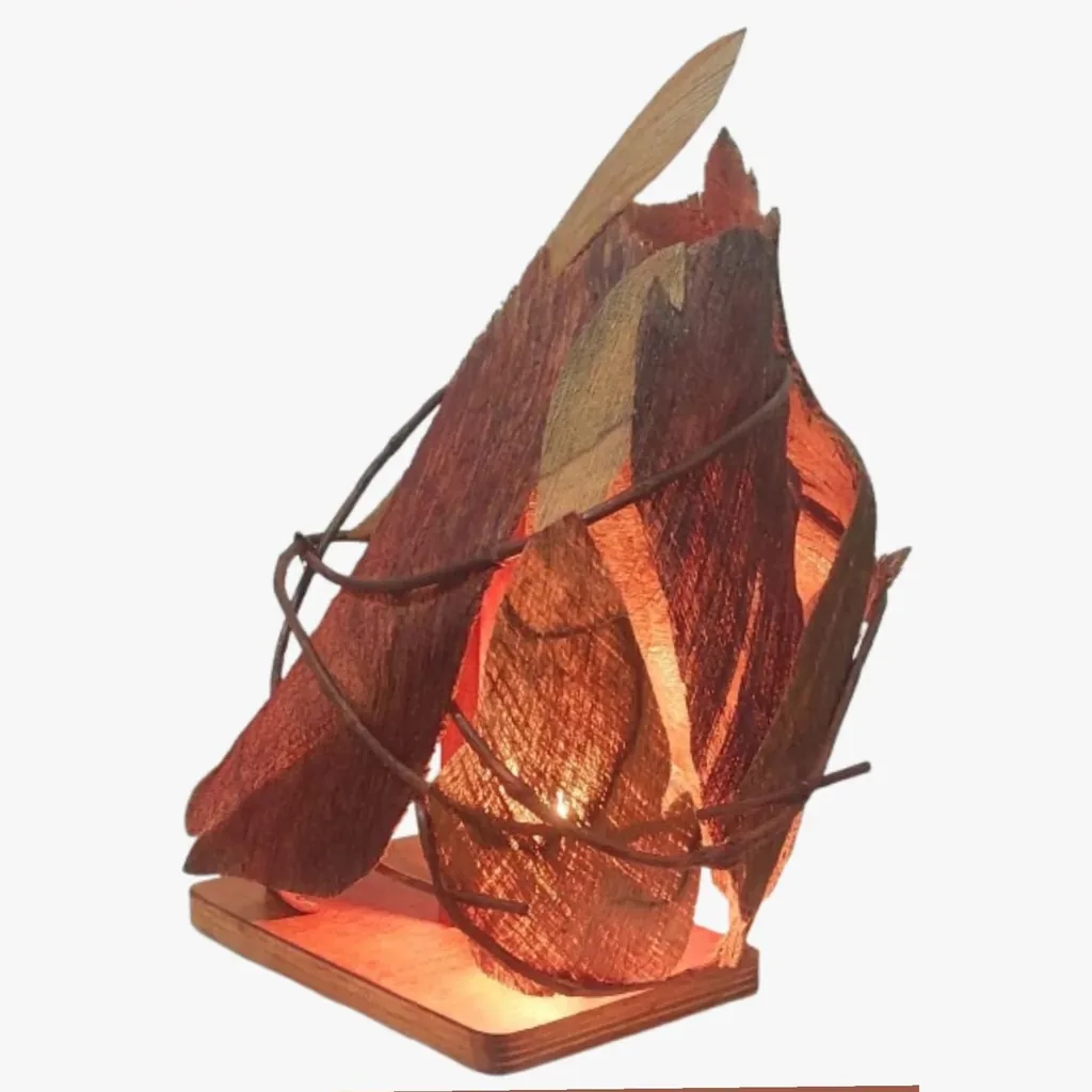 Luminária de mesa de folhas e fibras amarradas com cipó, acesa, sobre base de madeira