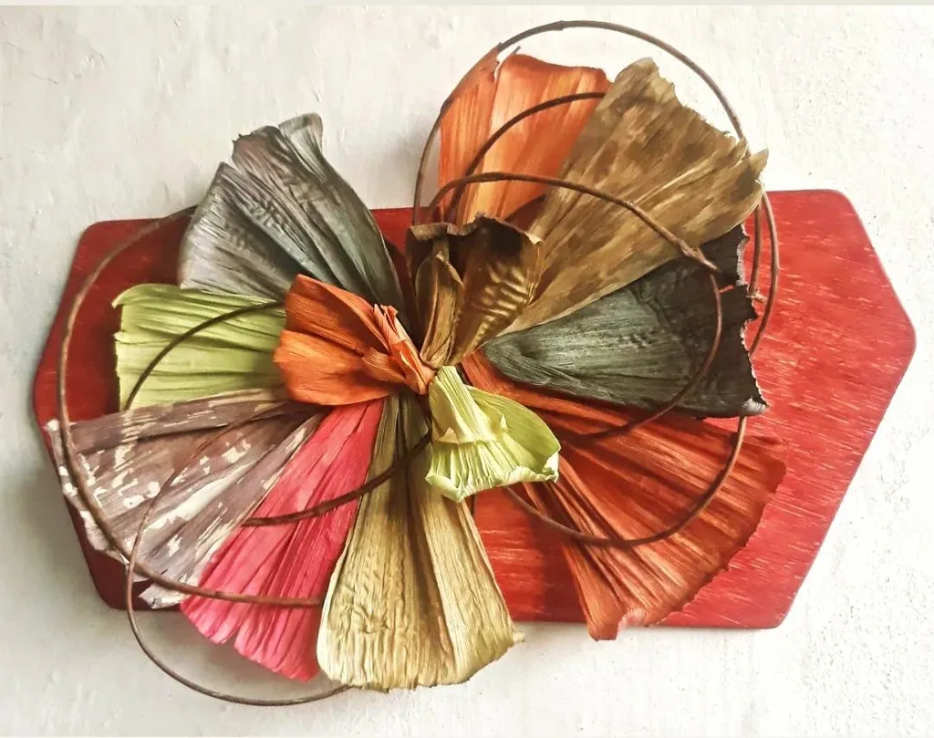 Peça de parede feita de palhas coloridas em leque, com aros de cipó, sobre base vermelha